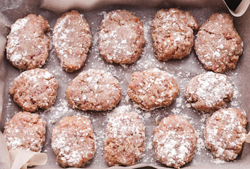 fresh minced raw meat cutlets on tray with flour on parchment, view from above