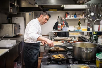 Papier Peint photo autocollant Cuisinier Beau chef cuisinier en uniforme cuisinant des aliments sur la cuisinière à gaz dans la cuisine du restaurant ..