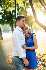 Naklejka premium beautiful couple in love with a woman walking in a park on a bench kissing at sunset and loving each other, a blue dress and a white shirt with jeans