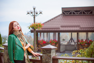 Girl with red hair, dressed in a green leather jacket and scarf casual style, resting in a pleasant place is in a sense of peace and harmony. Beauty in every day and moment, the pleasure of life