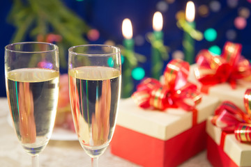 on the table are two glasses of champagne. near there are New Year's gifts. background - burning candles on a dark blue background with blurred lights. horizontal