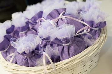 Bomboniere viola con confetti per celebrazioni dentro a cesta di vimini bianco