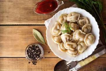 Russian meat dumplings pelmeni with dill on wooden rustic background.