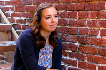 Fototapeta na wymiar Girl Sitting on Stairway, Next to Red Brick Wall