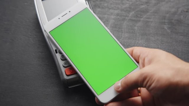 Top view of person using contactless payment with smartphone. Green screen template on phone.