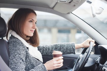 Young woman driving car in the city holding coffee to go