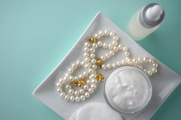 A jar of luxury beauty face cream and serum bottle with pearls teal mint aqua turquoise blue on color background with copy space. Styled feminine lifestyle image.
