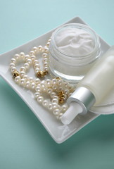 A jar of luxury beauty face cream and serum bottle with pearls teal mint aqua turquoise blue on color background with copy space. Styled feminine lifestyle image.
