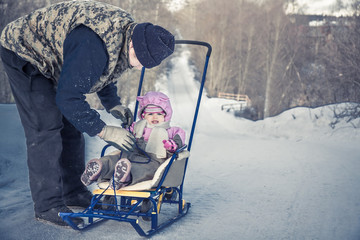 Obraz na płótnie Canvas Active senior adult man with his granddaughter sledding in winter park in snowy weather during winter holidays