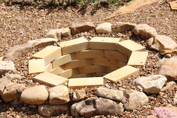Fire pit made of the yellow aluminous bricks and boulders surrounded by pebbles in the summer garden