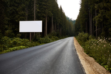 Blank billboard sign by empty highway through forest mountains landscape. Ad panel on road. © Aleksey
