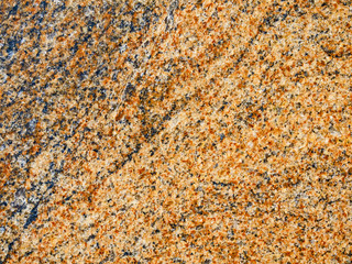 A close-up of a surface of treated red granite rock plate. A fragment of a stone wall decoration. Texture of bright red to orange granite facing material.