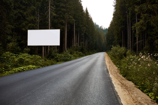 Blank billboard sign by empty highway through forest mountains landscape. Ad panel on road.