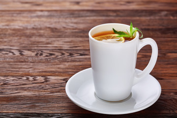 Tea with lemon in white cup, cinnamon sticks, knitted woolen scarf on wooden table