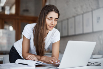 Cheerful beautiful woman using laptop computer in open coworking studio space. Browsing social networks.