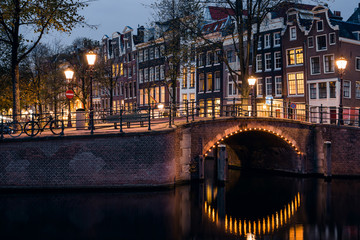 A bridge, canal, historic houses, and yellow light trail during twilight blue hour, Amsterdam, Netherlands