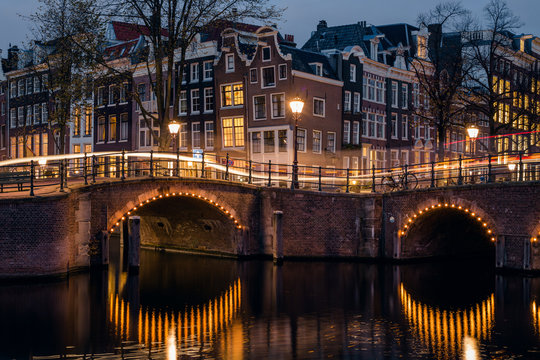 Old Historic Houses, Canal, Bridge And A Yellow Light Trail During Twilight Blue Hour, Amsterdam, Netherlands