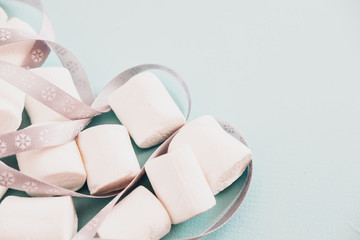 marshmallows and gray ribbon on light pastel blue background