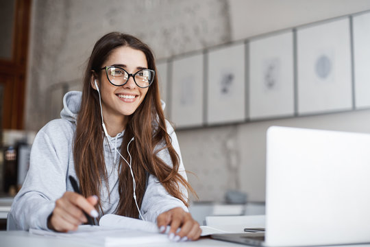 Young female teacher wearing glasses preparing for her class listening to upbeat music using laptop computer smiling laughing.