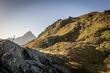 Wanderweg mit Steine im Vordergrund und Gipfel im Hintergrund beim Sonnenaufgang