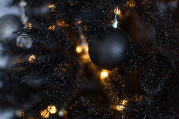 Christmas dark blurred background with a black Christmas tree, ornaments and bokeh lights