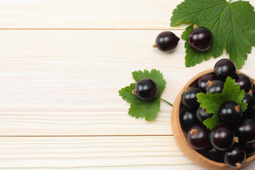 black currant in wooden bowl with green leaf on white wooden background. top view with copy space
