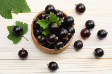 black currant in wooden bowl with green leaf on white wooden background. top view with copy space