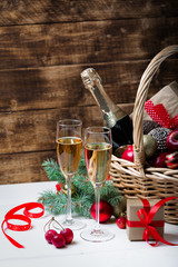 Two glasses of champagne with christmas basket with bottle, gifts with red satin ribbon, candy...