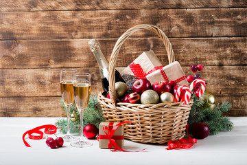 Two glasses of champagne with christmas basket with bottle, gifts with red satin ribbon, candy...