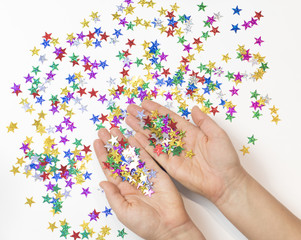 Female Hands Covered with Colorful Stars Confetti White Background. Christmas Celebration Fairy Tale Concept. Top View Flat Lay Copy Space