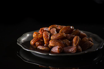 Sweet dessert dried date in old tin bowl, low key, dark theme, on black background with reflection copy space
