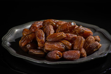Sweet dessert dried date in old tin bowl, low key, dark theme, on black background with reflection
