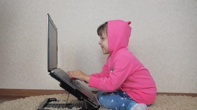 Angry child with laptop. A little girl in a pink hood is working on a laptop.