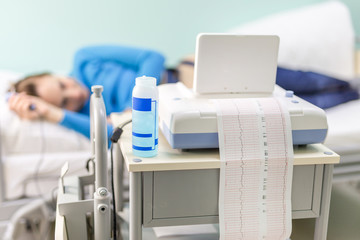 Young happy woman lying on a bed in a hospital while doctor setting a cardiotocography sensor to...