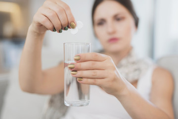 Sick pregnant woman sitting at home on the couch. She throws two tablets into a glass of water
