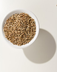 Rye cereal grain. Grains in a bowl. Shadow over white table.