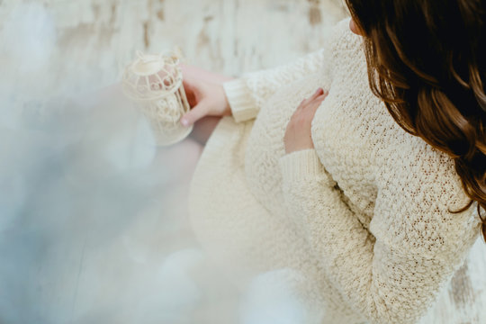 Pregnant girl in a knitted sweater beige color sitting on floor and holding a small cell