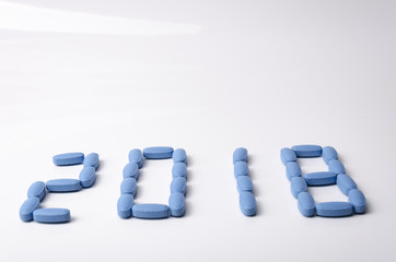 Creative 2018 new year concept made out blue medical tablets over a white background.
