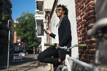 Afro young man using mobile phone and fixed gear bicycle.