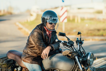Motorcyclist sits on an old cafe-racer motorcycle, autumn background