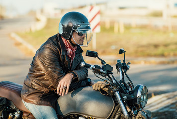 Fototapeta premium Motorcyclist sits on an old cafe-racer motorcycle, autumn background