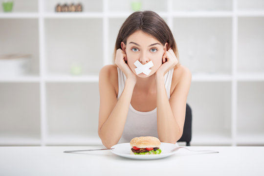 Diet. Young woman with duct tape over her mouth, preventing her to eat junk food. Healthy eating concept
