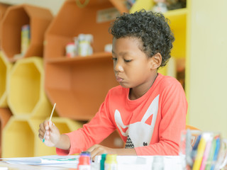 American boy make home wore drawing color pencils in kindergarten classroom, preschool library and...