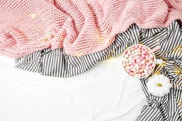 Cup of coffee and marshmallow on bedding with fairy lights. Copy space. Flat lay, top view