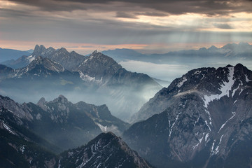 Sun rays illuminate autumn morning mist and jagged peaks of Koschuta Kosuta and Begunjscica ridges in Karawanken Karavanke mountain and Kamnik Alps near Loibl Ljubelj pass, Austria / Slovenia border