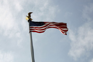 American flag topped with golden eagle blowing in the wind