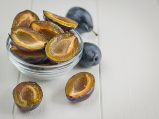Glass bowl full of ripe blue plums on white wooden table.