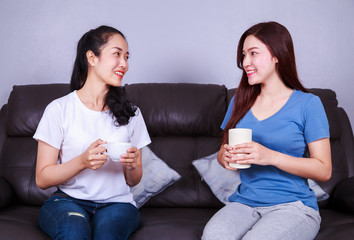 two best friends talking and drinking a cup of coffee on sofa in living room
