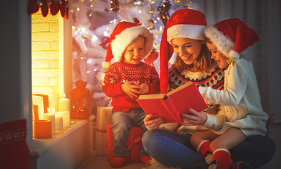 family mother and children read a book at christmas near   fireplace at home