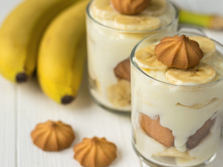Banana pudding in glasses with cookies on a white wooden table.